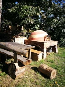 En primer plana mesa y banco hechos de madera y sin clavos; en segundo plano un horno de leña hecho de barro